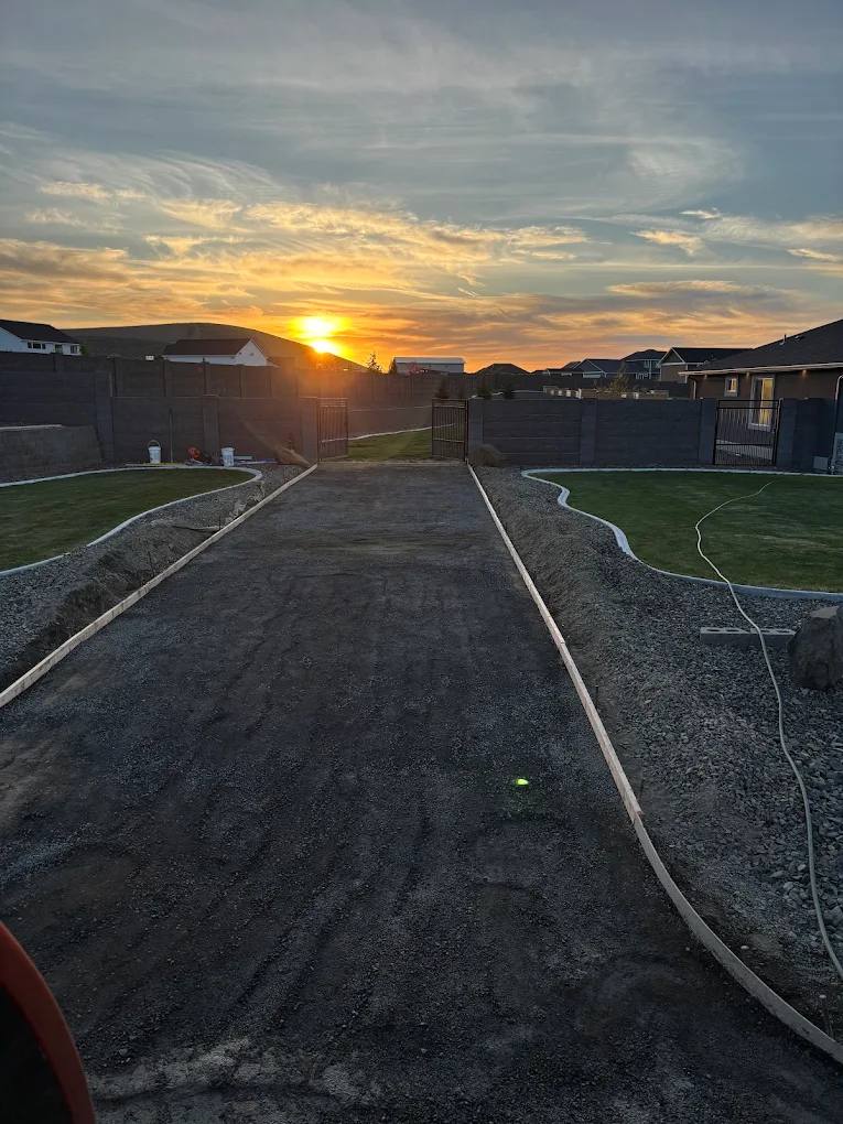 A graded and compacted gravel driveway base staked and ready for concrete, photographed at sunset