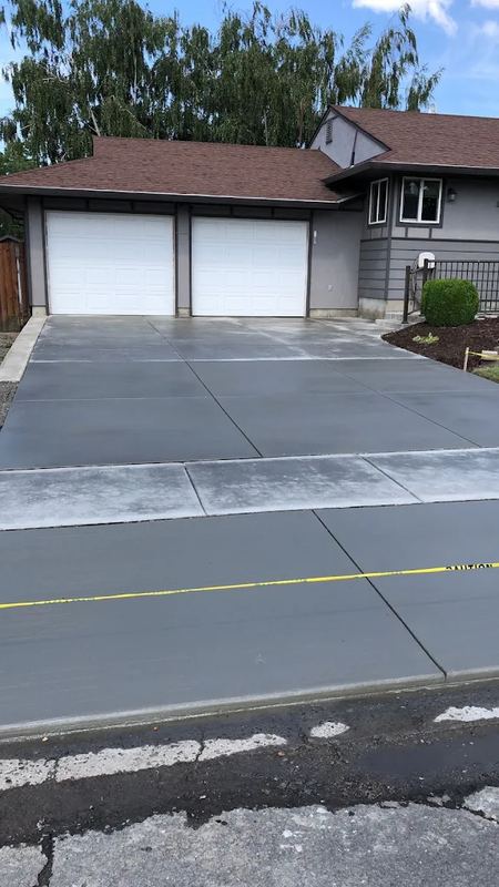 Freshly poured concrete driveway leading to a two-car garage, with the old asphalt edge still visible at the street