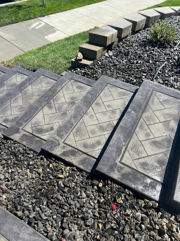 Stamped concrete steppers in a herringbone pattern bordering a lawn and rock bed