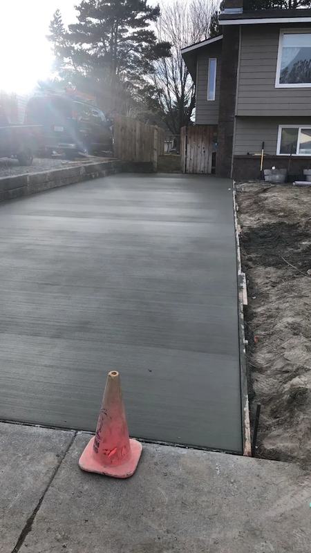Finished concrete driveway leading to a two-story home with an orange safety cone at the curb