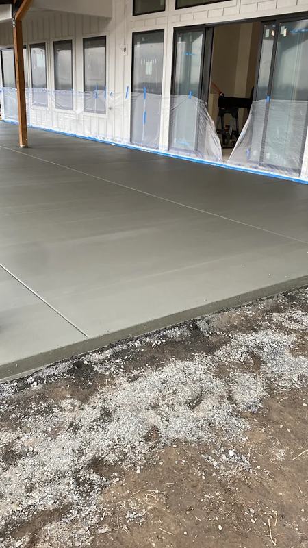 Finished concrete driveway and pad bordered by a white ranch-style fence