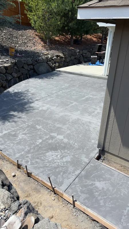 Curved concrete patio bordering a stacked stone retaining wall and lawn