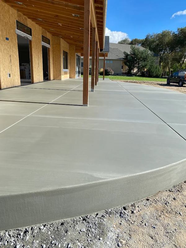 Large curved concrete patio under a wood pergola attached to a home