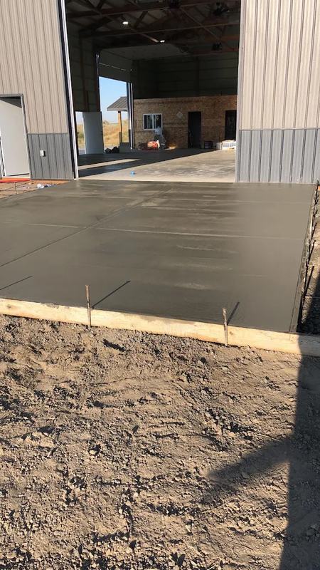 Freshly formed concrete slab in front of an open metal pole building