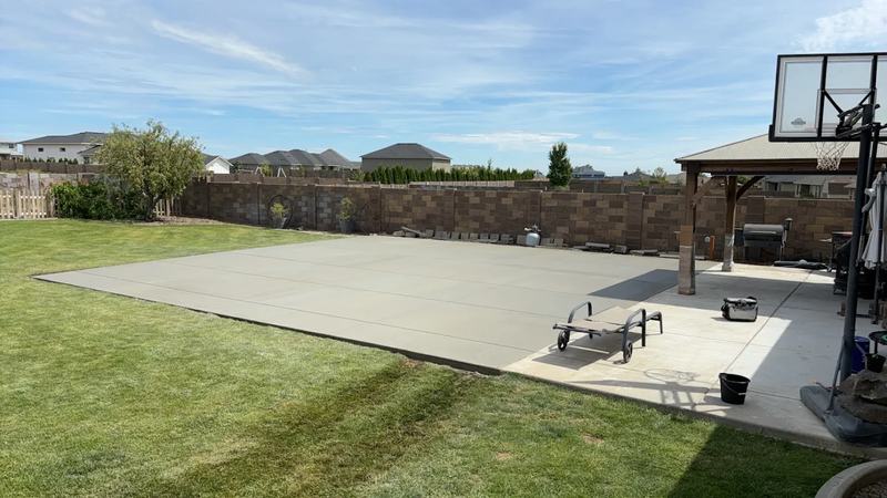 Large finished concrete slab in a backyard set up as a basketball court