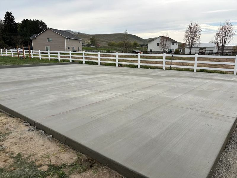 Large finished concrete pad bordered by a white ranch fence