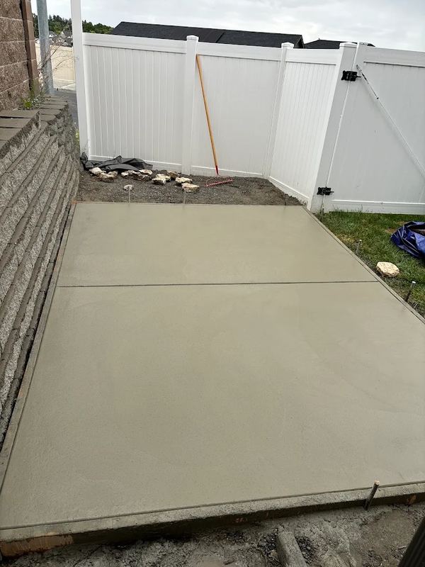 Finished backyard concrete patio next to a white vinyl fence